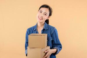 Portrait asian young woman wearing denim shirt holding parcel box isolated on beige studio background, Delivery courier and shipping service concept. photo