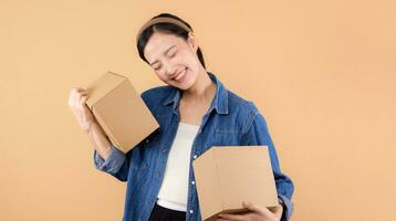 Portrait asian young woman wearing denim shirt holding parcel box isolated on beige studio background, Delivery courier and shipping service concept. photo