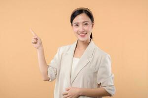 Studio portrait of happy successful confident young asian business woman. Beautiful young lady in white jacket smiling at camera standing isolated on solid beige colour copyspace background photo