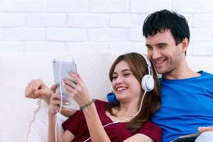 contento joven casado Pareja relajante juntos a hogar con el esposa acostado espalda en contra su marido como ella escucha a música en tableta. foto