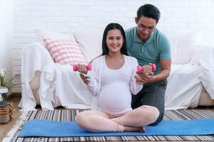 Husband take care his wife pregnant help exercise in living room at home. Pregnancy couple healthcare and relationship concept. photo