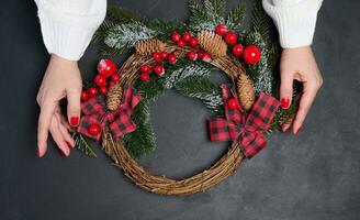 Two female hands holding a Christmas wreath on a black background, top view photo