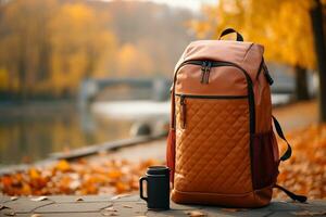 Backpack with a thermos in an autumn park near the river. Travel concept. Generated by artificial intelligence photo