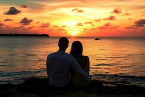 Caucasian couple sitting on rock near sea at sunset photo