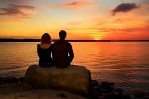 Caucasian couple sitting on rock near sea at sunset photo