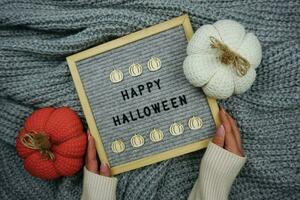 On a knitted gray background, a sign with the inscription happy Halloween and there are knitted pumpkins photo