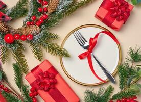 Empty round white plate with fork and wrapped gifts with Christmas decor on a beige background, top view. Festive background photo