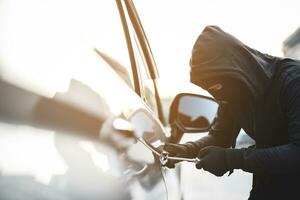 Close up car thief hand holding screwdriver tamper yank and glove black stealing automobile trying door handle to see if vehicle is unlocked  trying to break into inside. photo