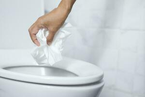 close up hand holding a tissue to be thrown into the toilet bowl. Can not drain water of toilet paper in the toilet bowl cause the stool to clog up. photo