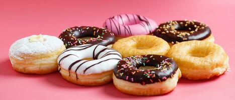 assorted donuts with chocolate frosting, topping sprinkles donuts Colorful variety and Variety of flavors mix of multi colored sweet donuts with frosted sprinkled on pink background. top view photo