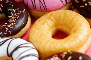 assorted donuts with chocolate frosting, topping sprinkles donuts Colorful variety and Variety of flavors mix of multi colored sweet donuts with frosted sprinkled on pink background. top view photo