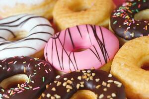 assorted donuts with chocolate frosting, topping sprinkles donuts Colorful variety and Variety of flavors mix of multi colored sweet donuts with frosted sprinkled on pink background. top view photo