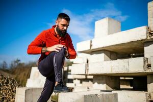 Adult man is exercising outdoor on sunny day. He is stretching his body. photo