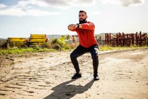 Young man is exercising outdoor. He is doing squats. photo