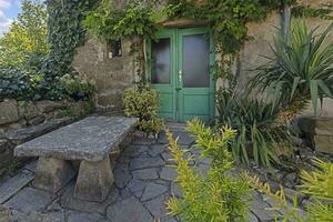 Image of an entrance area to an ancient house with climbing plants and a stone resting place photo