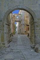 ver mediante un arqueado puerta a lo largo un adoquinado calle dentro un antiguo pueblo sin personas foto