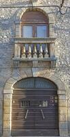 Image of a brown entrance door to a residential building with a stone balcony and window with shutters on a antique facade photo