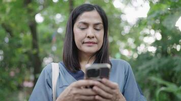 vrouw chatten Aan cel telefoon terwijl staand De volgende naar struiken video