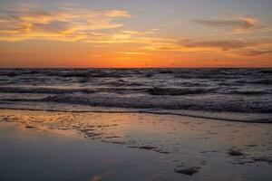 A peaceful, meditative sunset, white waves in the sea and orange-yellow clouds photo