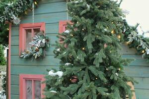 Frosted window sill with christmas decoration. Winter holiday home, view from outdoors. Fir tree garland on wooden board of front yard facade house. New Year festive decor of the streets photo