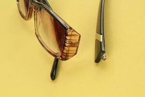 Old broken eyeglasses with damaged legs on orange background. Poor eyesight. Reuse and repair concept. Idea of health. Failure optic eyewear. Breakage of vision correction glasses. Close up, flat lay photo