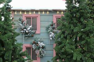 Frosted window sill with christmas decoration. Winter holiday home, view from outdoors. Fir tree garland on wooden board of front yard facade house. New Year festive decor of the streets photo