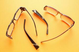 Old broken eyeglasses with damaged legs on orange background. Poor eyesight. Reuse and repair concept. Idea of health. Failure optic eyewear. Breakage of vision correction glasses. Close up, flat lay photo