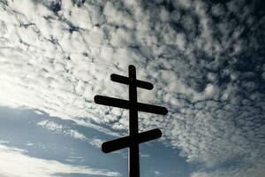 Cross on top of a hill against a blue sky with white clouds. Silhouette of a cross in the field at sunset with dramatic sky. photo