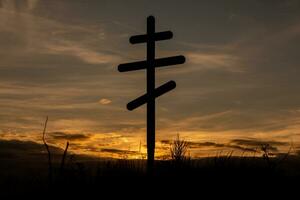 Cross on top of a hill against a blue sky with white clouds. Silhouette of a cross in the field at sunset with dramatic sky. photo