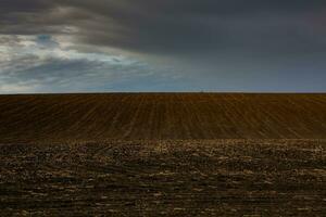 Plowed field with tractor on the horizon and dark clouds in the sky photo