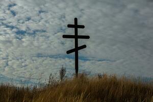 Cross on top of a hill against a blue sky with white clouds. Silhouette of a cross in the field at sunset with dramatic sky. photo