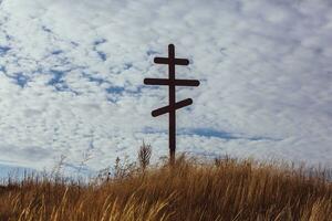 Cross on top of a hill against a blue sky with white clouds. Silhouette of a cross in the field at sunset with dramatic sky. photo