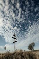 cruzar en parte superior de un colina en contra un azul cielo con blanco nubes silueta de un cruzar en el campo a puesta de sol con dramático cielo. foto