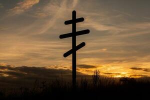 Cross on top of a hill against a blue sky with white clouds. Silhouette of a cross in the field at sunset with dramatic sky. photo