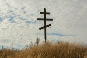 Cross on top of a hill against a blue sky with white clouds. Silhouette of a cross in the field at sunset with dramatic sky. photo