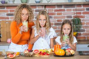 Mother and daughters cooking together in the kitchen. Healthy food concept. Portrait of happy family with fresh smoothies. Happy sisters. photo