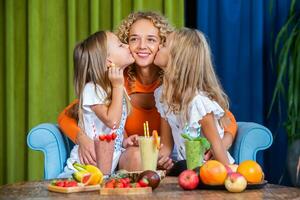 Mother and daughters cooking together in the kitchen. Healthy food concept. Portrait of happy family with fresh smoothies. Happy sisters. photo