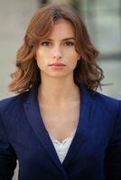 Portrait of a successful business woman in front of modern business building. Young manager poses outside. Woman employee of an office. photo