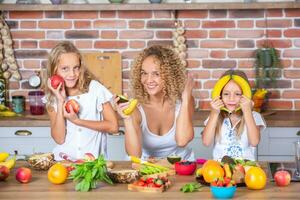 Mother and daughters cooking together in the kitchen. Healthy food concept. Portrait of happy family with fresh smoothies. Happy sisters. photo