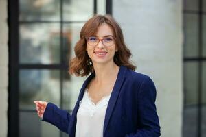 Portrait of a successful business woman in front of modern business building. Young manager poses outside. Woman employee of an office. photo