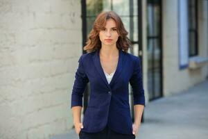 Portrait of a successful business woman in front of modern business building. Young manager poses outside. Woman employee of an office. photo