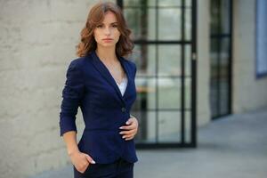 Portrait of a successful business woman in front of modern business building. Young manager poses outside. Woman employee of an office. photo