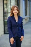 Portrait of a successful business woman in front of modern business building. Young manager poses outside. Woman employee of an office. photo