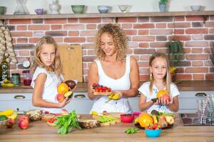 Mother and daughters cooking together in the kitchen. Healthy food concept. Portrait of happy family with fresh smoothies. Happy sisters. photo
