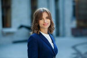 Portrait of a successful business woman in front of modern business building. Young manager poses outside. Woman employee of an office. photo