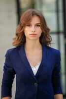 Portrait of a successful business woman in front of modern business building. Young manager poses outside. Woman employee of an office. photo