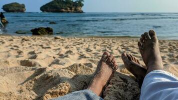 The couple is enjoying their vacation at the beach, lying on the sand and looking out at the ocean. The couple's feet are covered in beach sand. Summer and beach concept. photo