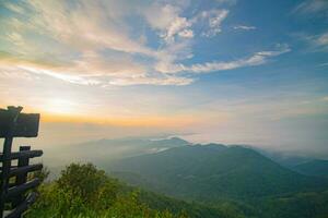 The stunning view from a tourist's standpoint as they go down a hill on a foggy trail with a hill and a background of a golden sky in Forest Park, Thailand. Bird's eye view. Aerial view. photo