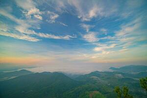 The stunning view from a tourist's standpoint as they go down a hill on a foggy trail with a hill and a background of a golden sky in Forest Park, Thailand. Bird's eye view. Aerial view. photo