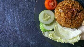 Copiar espacio de nasi goreng o frito arroz, indonesio calle alimento, complementado pepino, galletas saladas, Tomates, y repollo rociado con frito cebollas con plano laico y oscuro antecedentes foto